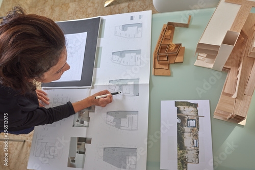  Young woman works as an architect in an office. She is brunette and Latina has a black shirt and different jobs on her table.