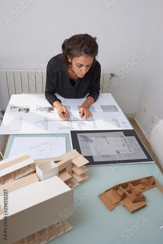  Young woman works as an architect in an office. She is brunette and Latina has a black shirt and different jobs on her table.