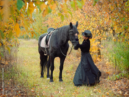 horsewoman girl in a black dress leads a black horse