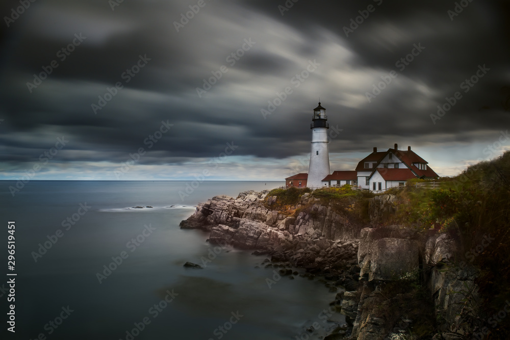 A lighthouse on a cliff on the shore of the Atlantic Ocean against a dramatic sky. Long exposure. Maine's oldest lighthouse. Portland USA.