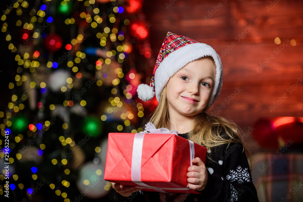 Kid adorable wear santa hat celebrate christmas. Buy christmas gift. Winter shopping. Girl cute child hold wrapped gift near christmas tree. Holiday party that actually sounds fun. Merry christmas