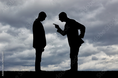 Silhouette of a standing man screaming at a standing man with his head bowed against a cloudy sky