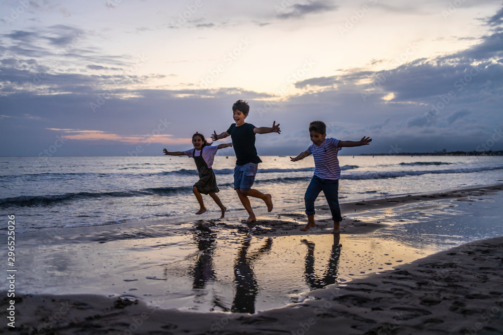 Three kids running on the beach at sunset