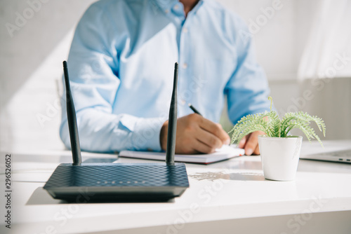 cropped view of businessman writing in notebook near router and flowerpot