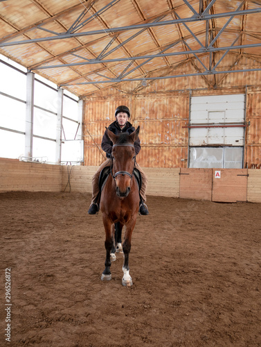 A man while riding a thoroughbred horse during training in the arena.