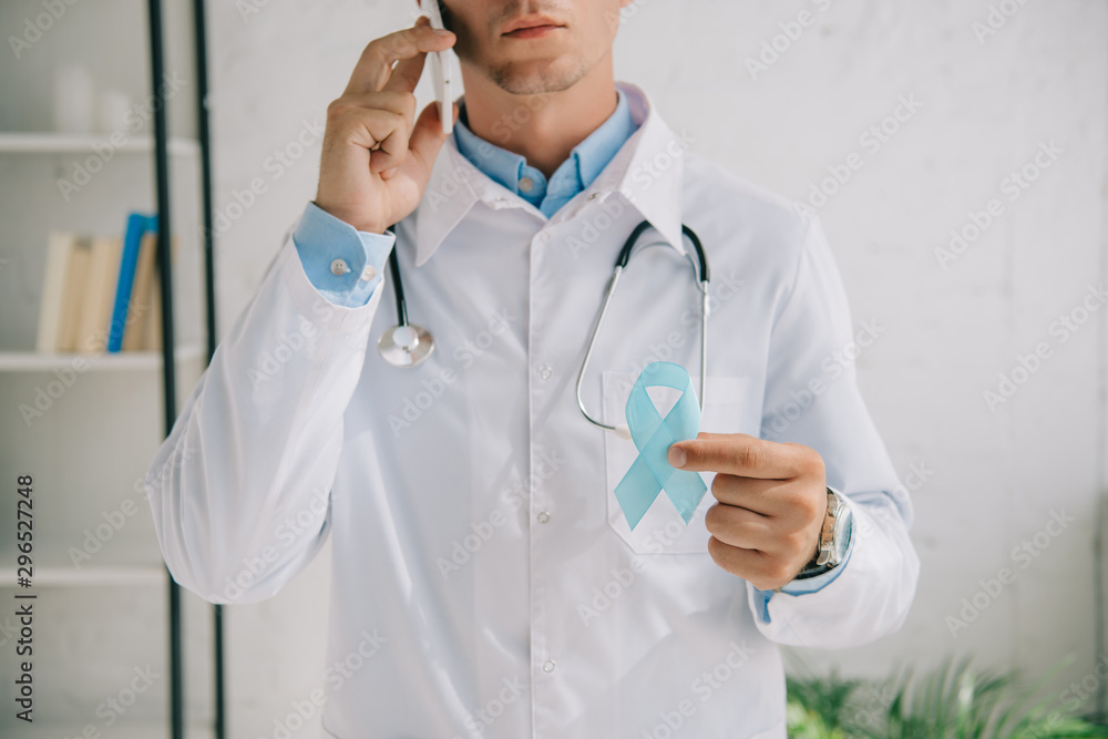 cropped view of doctor holding blue awareness ribbon while talking on smartphone cropped view of doctor holding blue awareness ribbon while talking on smartphone