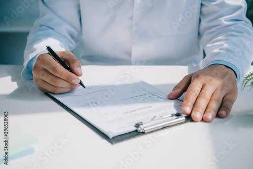 partial view of doctor writing diagnosis in medical report on clipboard