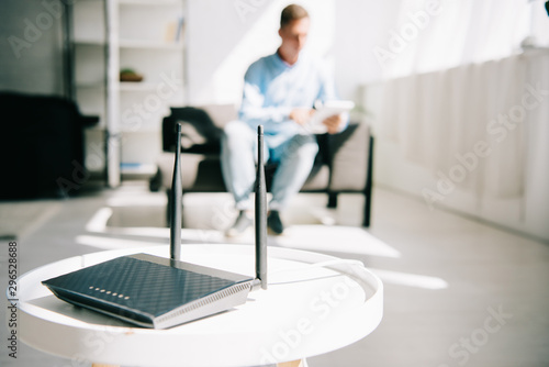selective focus of black plugged router on white table and businessman sitting on sofa photo