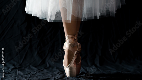 Fotografia Close-up of dancing legs of ballerina wearing white pointe on a black background