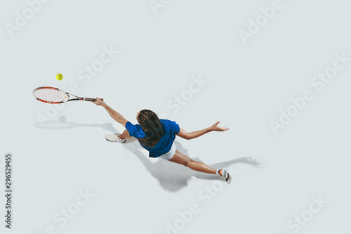 Young woman in blue shirt playing tennis. She hits the ball with a racket. Indoor studio shot isolated on white. Youth, flexibility, power and energy. Negative space. Top view.