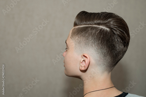 Stylish modern retro haircut side part with mid fade with parting of a school boy guy in a barbershop on a brown background photo