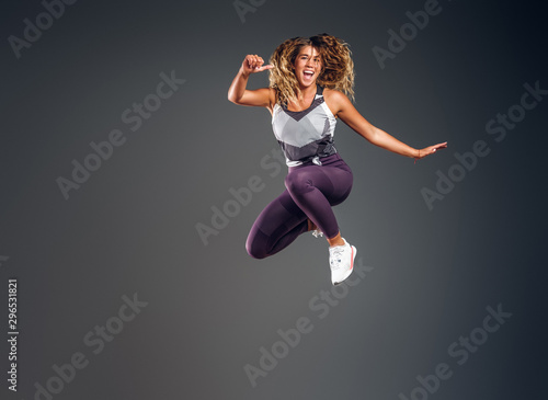 Cheerful happy woman is showing her performance at photo studio on the grey background.