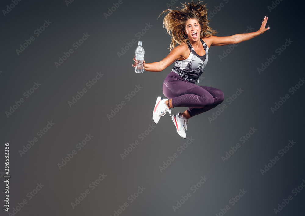 Joyful energising woman is jumping at photo studio with bolle of water making, splashes.