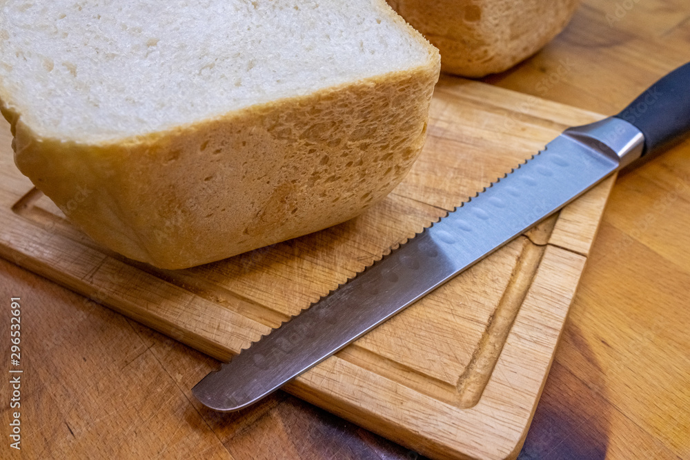 Freshly baked homemade bread cut in half on a wooden kitchen board and lying next to a bread knife for cutting bread.