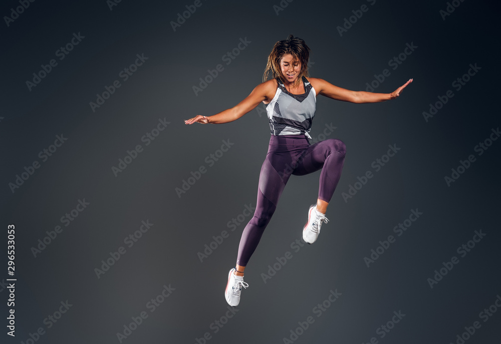 Happy attractive woman in activewear is jumping at studio over grey background.