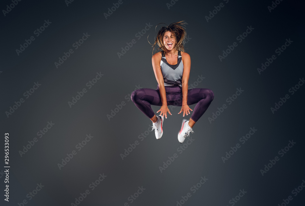 Happy attractive woman in activewear is jumping at studio over grey background.