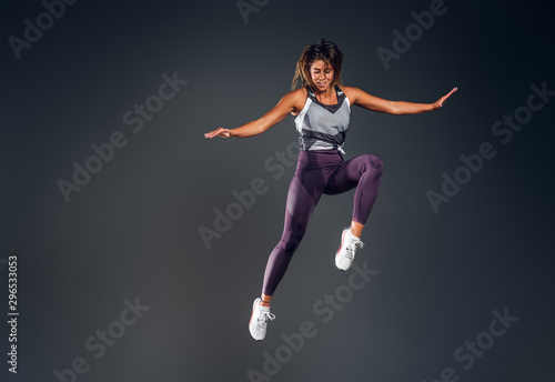 Fototapeta Naklejka Na Ścianę i Meble -  Happy attractive woman in activewear is jumping at studio over grey background.