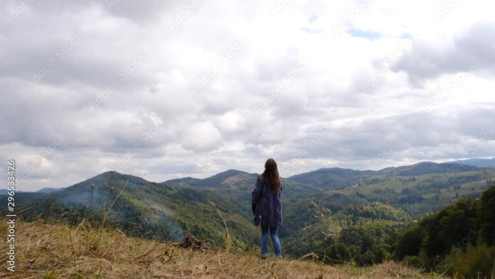 Rear view of young woman walks across the field and throws her hat on background top of mountain summit, raises hands into air, youth and happiness. Explore travel real wilderness lifestyle Rear view of young woman walks across the field and throws her hat on background top of mountain summit, raises hands into air, youth and happiness. Explore travel real wilderness lifestyle