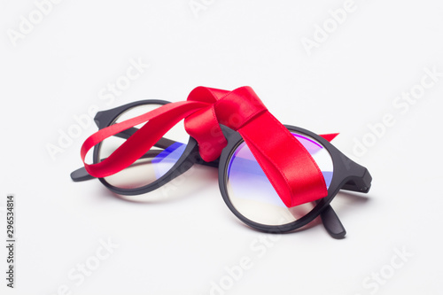 Gafas clásicas con cristales graduados, montura de plástico de color negro, sobre fondo negro con cinta de regalo de color rojo