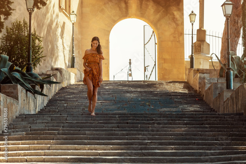 young brunette woman wearing a floral pattern summer dress, walking down a staircase, at a castle in Artà on Mallorca © farec