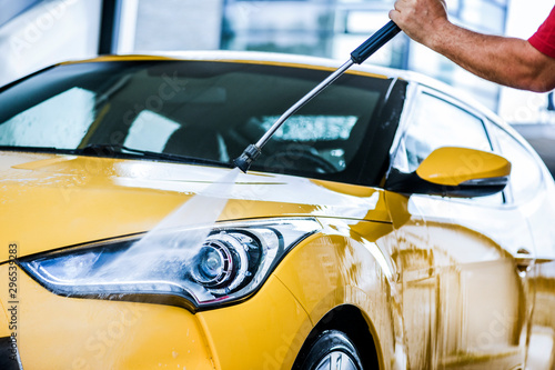 Man cleaning vehicle with high pressure water jet. Car wash details or close up.