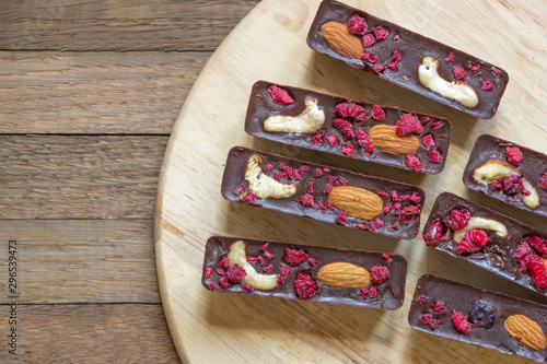 Delicious raw foods dessert from natural chocolate, cashew, almond and raspberry. Sweet sticks lay on round kitchen board on wooden background with copy space. Dietary tea treat. Healthy meal concept.