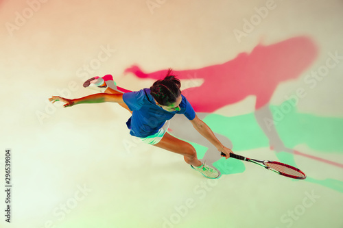 Young woman in blue shirt playing tennis. She hits the ball with a racket. Indoor studio shot with mixed light. Youth, flexibility, power and energy. Top view. © master1305