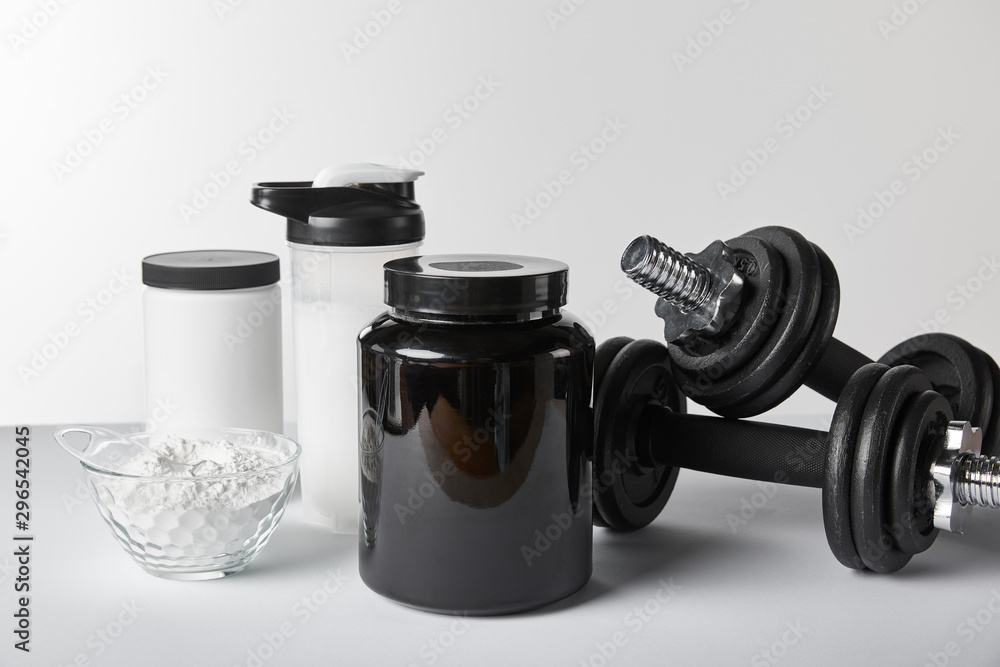 heavy dumbbells near jars and sports bottle with protein shake on white heavy dumbbells near jars and sports bottle with protein shake on white