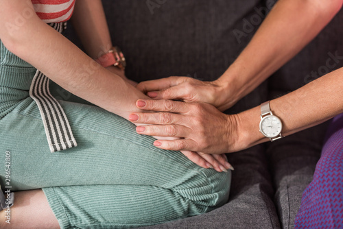 cropped view of woman touching hands of young daughter while sitting on sofa together