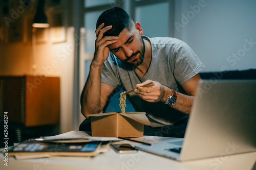 man working late on laptop eating chinese food at his home