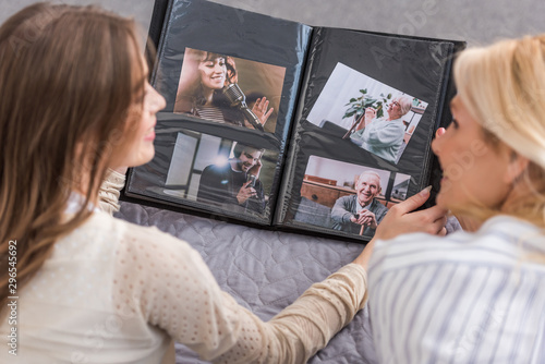 overhead view of mother and daughter talking while lying on bed and looking at photo album