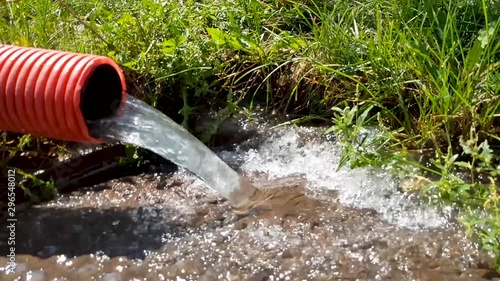 water from a red corrugated pipe flows down the drain. Water is flowing. Rain water flows out of the pipe and falls down. Wastewater flows into the external sewer. Pumping water with a pump
