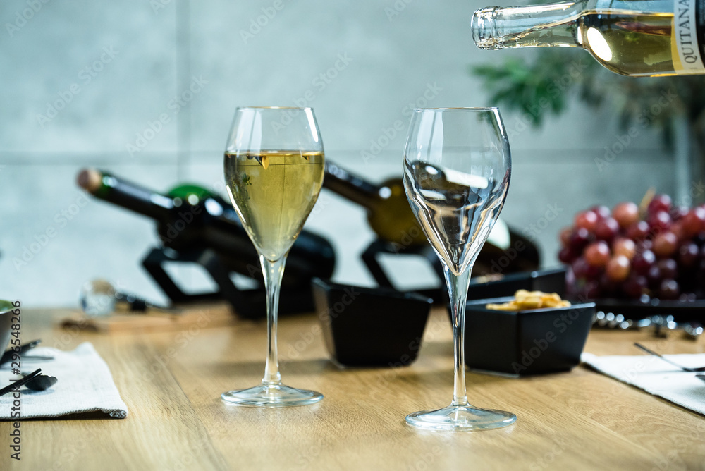 Obraz premium Pouring white wine into the glass against wooden table