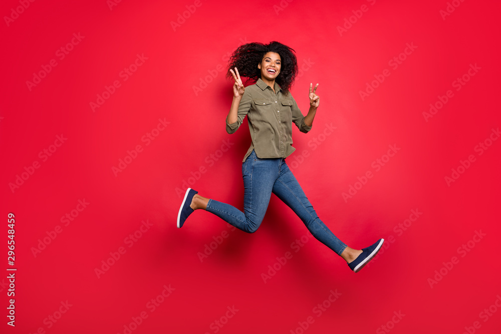 Full length body size photo of cheerful positive curly wavy brunette funky girlfriend running jumping showing v-sign wearing jeans denim shirt smiling toothily isolated vivid color background Full length body size photo of cheerful positive curly wavy brunette funky girlfriend running jumping showing v-sign wearing jeans denim shirt smiling toothily isolated vivid color background