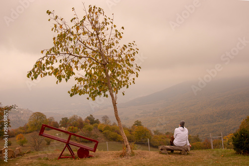 Autumn landscape.The girl sits on a bench on the hillside.Fields and mountains stretched before her.