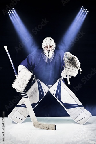 Hockey goalie stands in the spotlight ready to catch the puck.Hockey goalie in complete hockey gear  standing in front of black background. Above him are blue spotlight.
