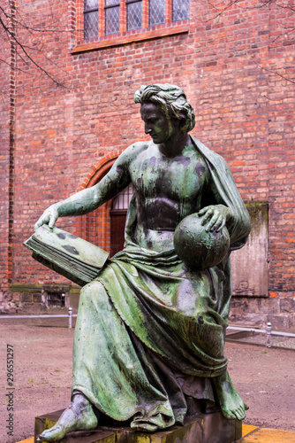 Bronze statue of The Allegory of Science, a man holding an open book and a globe, by Albert Wolff, with the Nikolaikirche behind in Nikolas' Quarter of Berlin