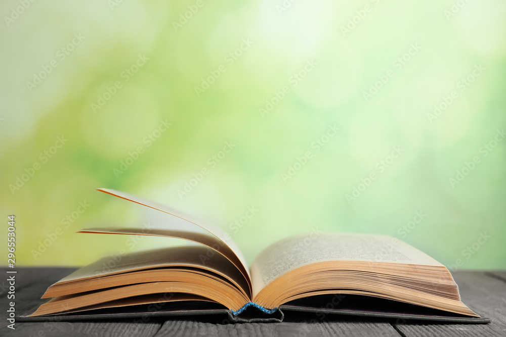Fototapeta premium Open book on blue wooden table against blurred green background. Space for text