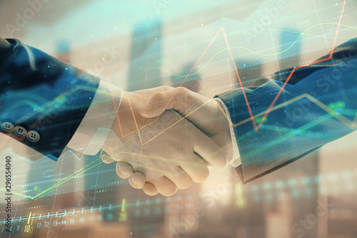 Double exposure of financial graph on cityscape background with two businessman handshake. Concept of stock market deal