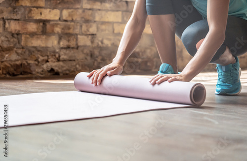Woman rolling yoga pilates rubber mat on gym studio floor, female fit sporty lady preparing for sport workout exercise fitness class close up view, training routine equipment background concept