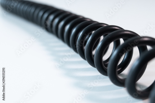 Black coiled cable on white table, diagonal right to left. Close up with shallow depth of field.