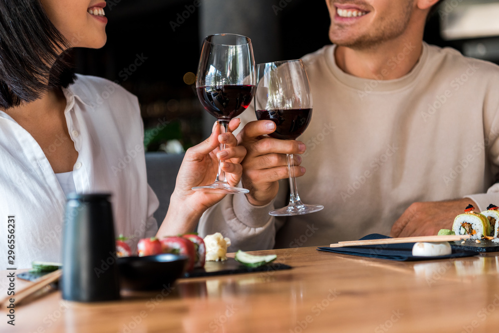 Cropped view of happy man and cheerful woman clinking glasses with red wine near sushi Cropped view of happy man and cheerful woman clinking glasses with red wine near sushi