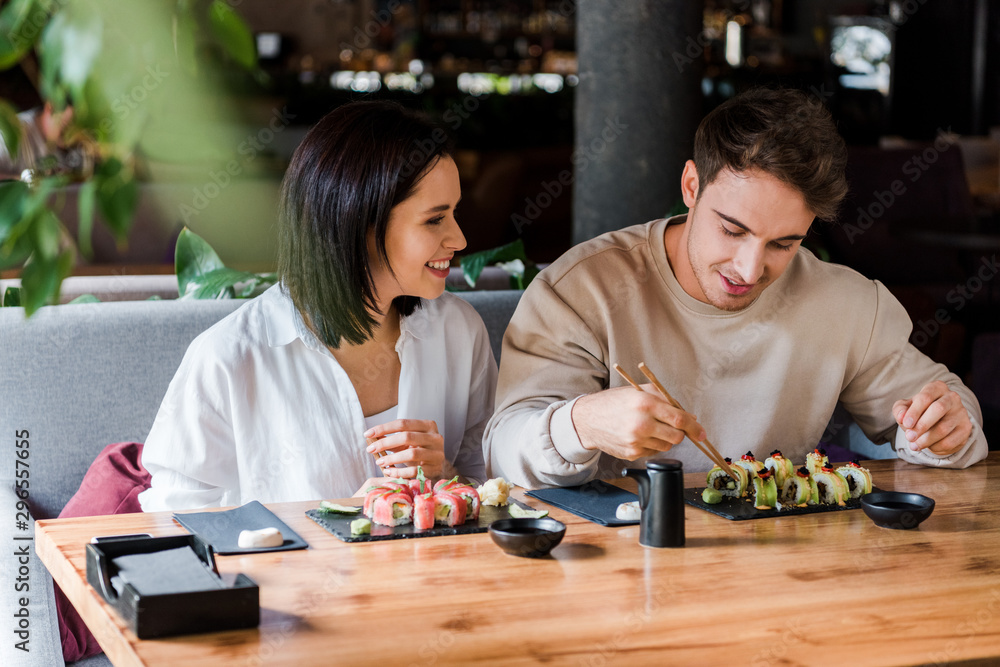 Fototapeta premium selective focus of happy man and woman near tasty sushi in restaurant