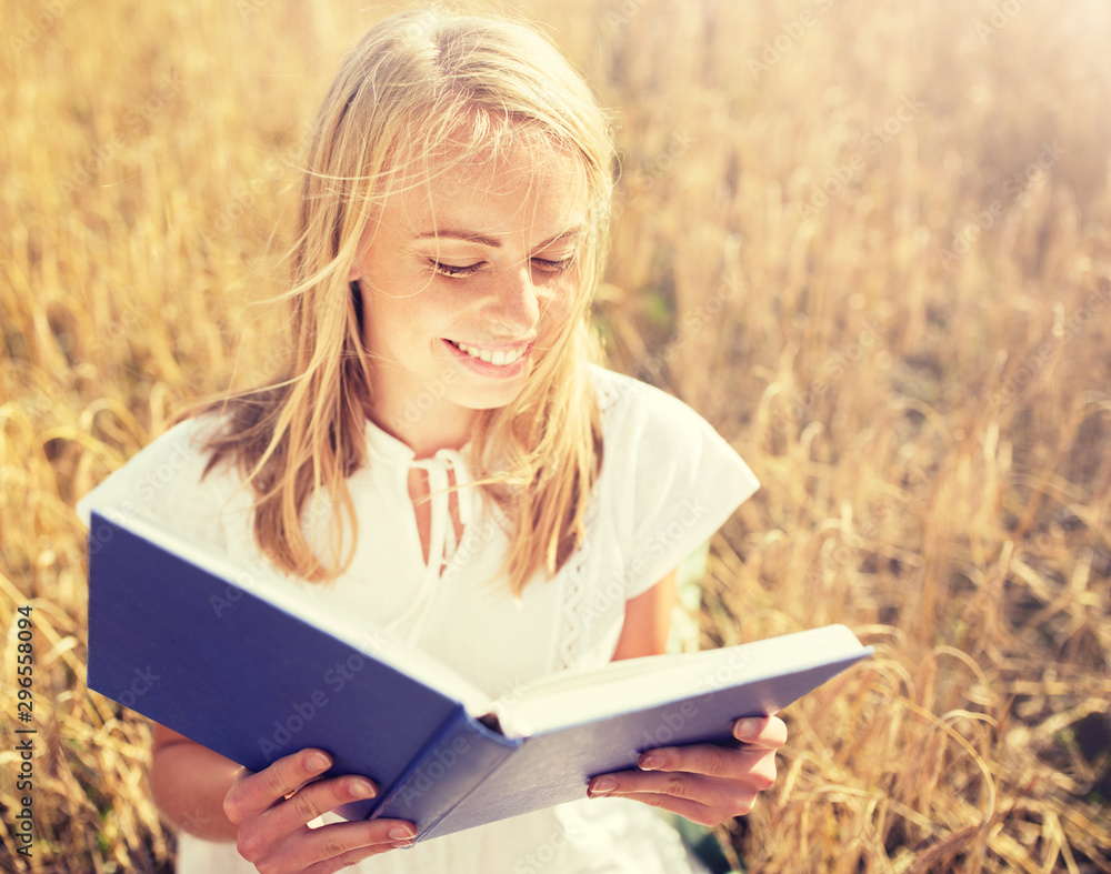 country, summer holidays, literature and people concept - smiling young woman in white dress reading book on cereal field country, summer holidays, literature and people concept - smiling young woman in white dress reading book on cereal field