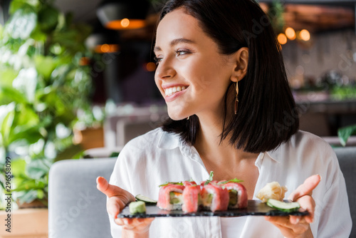 cheerful woman holding plate with tasty sushi in restaurant