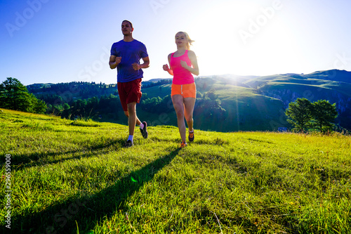 Running fitness couple of runners doing sport on road outdoor. Active living man and woman jogging training cardio in summer outdoors nature.