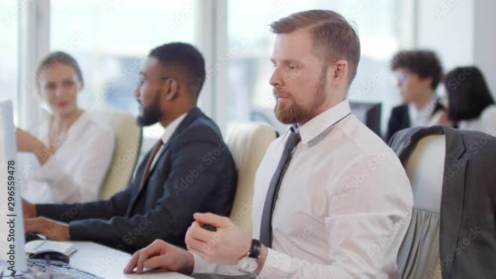 Lockdown of businesspeople sitting at desks, working while Caucasian businessman starting warming up his hands using expander while sitting on office chair and then continuing typing on keyboard Lockdown of businesspeople sitting at desks, working while Caucasian businessman starting warming up his hands using expander while sitting on office chair and then continuing typing on keyboard