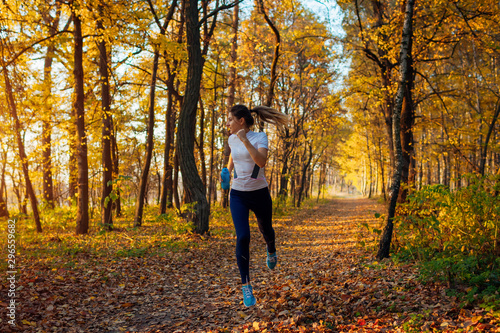 Runner exercising in autumn park. Woman running with water bottle at sunset. Active lifestyle