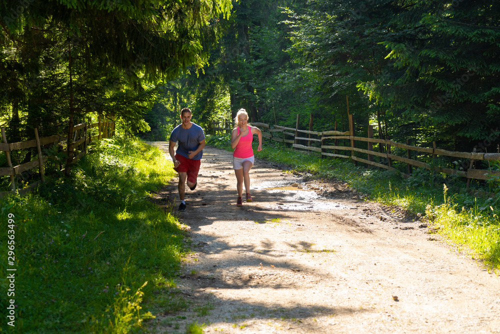 Obraz premium Running fitness couple of runners doing sport on road outdoor. Active living man and woman jogging training cardio in summer outdoors nature.