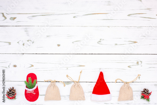 Weihnachtsdekoration mit drei Jutesäcke, Weihnachtsmütze, Tannenzapfen und roten Hausschuh mit Tannenzweig auf einem Holz Hintergrund